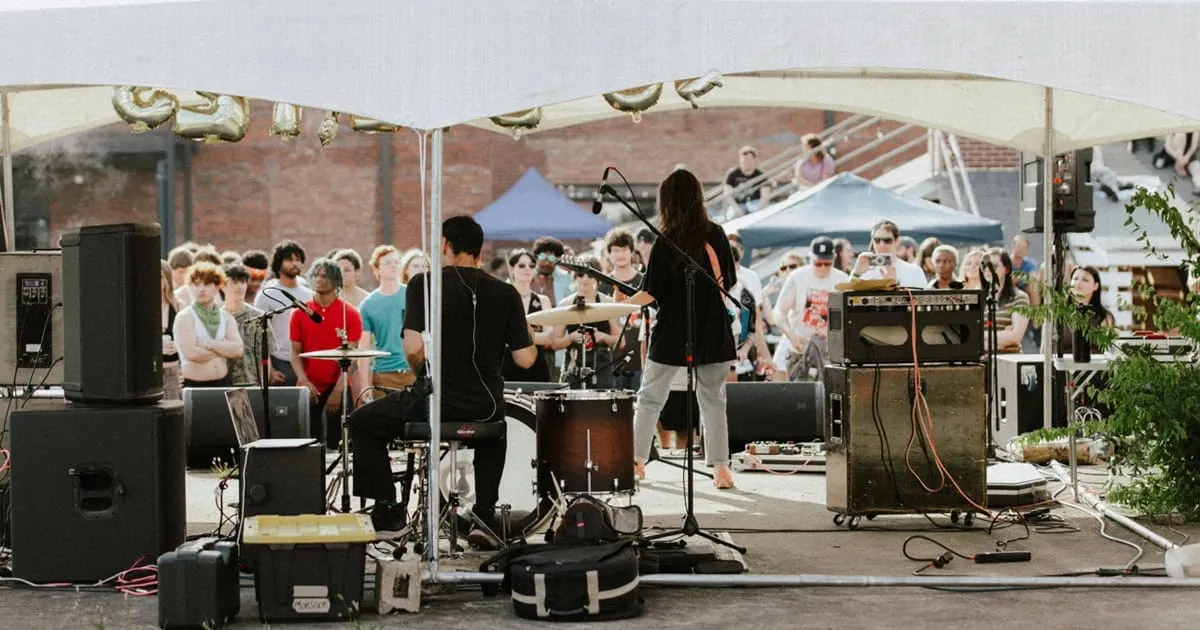 Live outdoor concert performance at a music festival with band playing under a tent, audience enjoying the music, vibrant atm