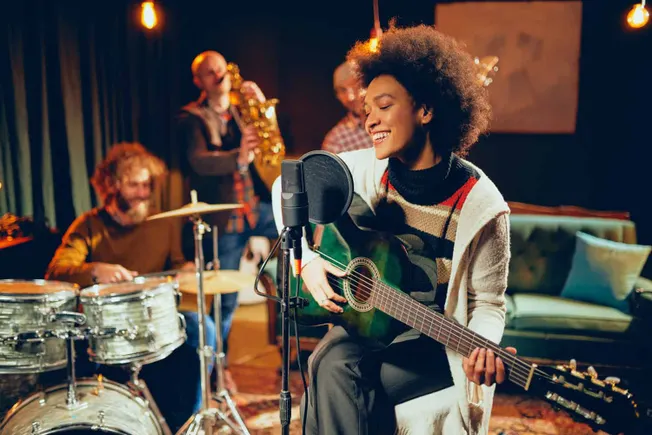 Young woman performing guitar and singing with a band of jazz musicians in a cozy studio.
