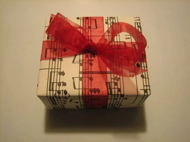 Gift box wrapped with musical notes and red ribbon, musical-themed present for music lover, artistic gift wrapping related to