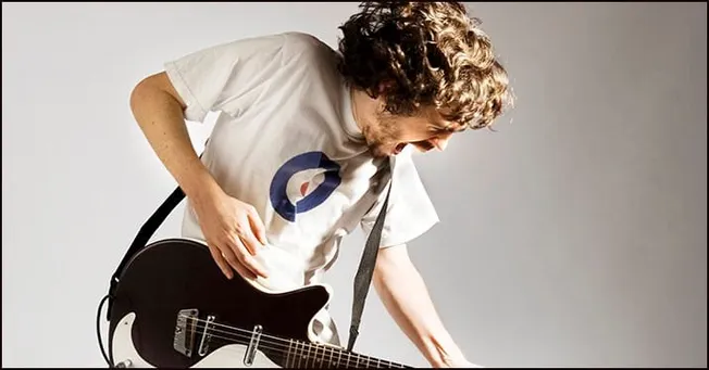 Guitarist playing guitar passionately, wearing a white t-shirt with a logo, engaging in music performance or practice.
