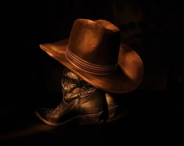 Cowboy boots with a wide-brimmed hat resting on top, dark background, Western wear style, rugged footwear, country fashion, o