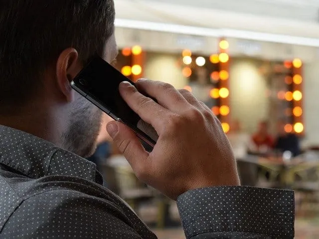 Man talking on mobile phone in a busy indoor setting with blurred background elements.