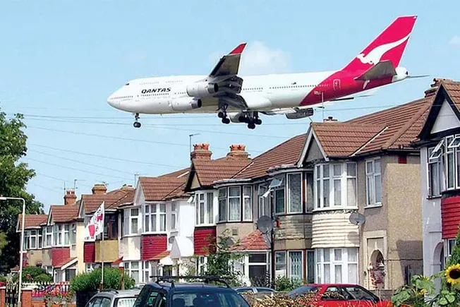 Qantas airplane flying low over residential neighborhood with houses and parked cars.