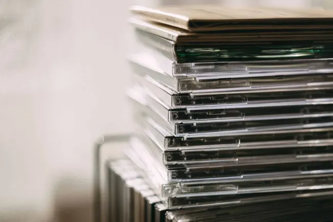 CD collection stacked vertically with some in jewel cases, representing music, media, or digital content.