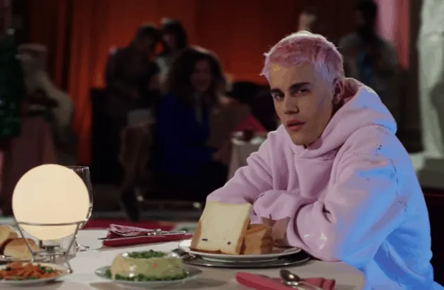 K-pop artist with platinum blonde hair wearing a pink hoodie at a restaurant table with food, popular in music and entertainm