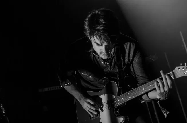 Guitarist playing electric guitar during live music performance in dark setting, black and white image.