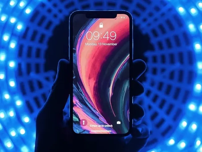 Smartphone with vibrant abstract wallpaper, illuminated by glowing blue LED lights in the background, showcasing modern mobil