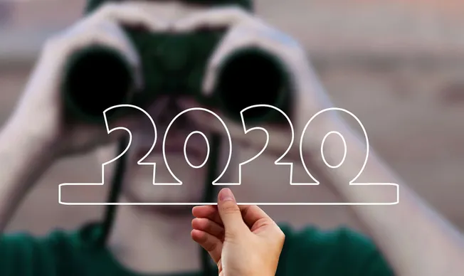 Colorful earbud headphones with a hand holding a sign displaying "2020" in front of a blurred outdoor background.