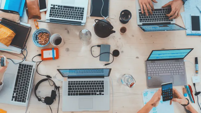 Laptops, smartphones, and office supplies on a wooden desk highlighting digital music marketing, streaming platform managemen