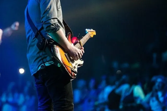 Electric guitar player performing on stage at a concert with blue lighting and audience in background, live music event, musi