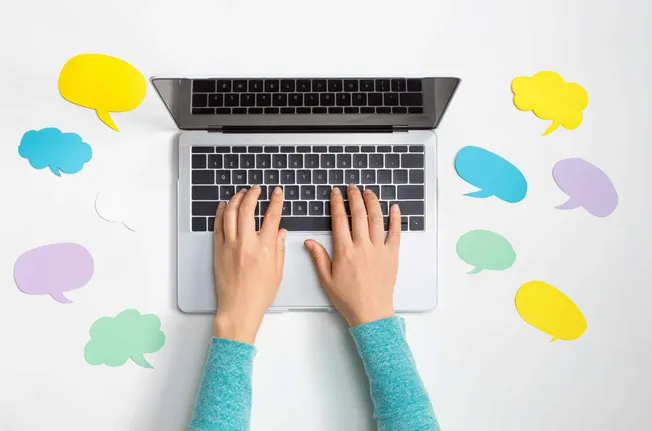 Typing on a silver laptop with colorful speech bubbles around it, symbolizing online communication, social media engagement,