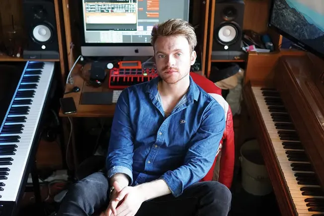 Young music producer sitting in a professional recording studio with keyboards and audio equipment, working on music producti