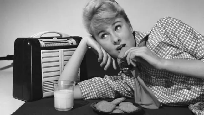 Disoriented woman with vintage radio, glass of milk, and cookies, illustrating retro style and nostalgic theme in black and w