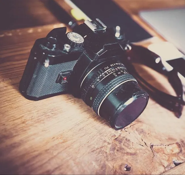 Camera with vintage lens on wooden surface, ready for photography, representing creative arts and photographic techniques.