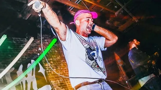 Hip hop artist performing energetically on stage with vibrant lights at a music event, showcasing live DJ performance, music