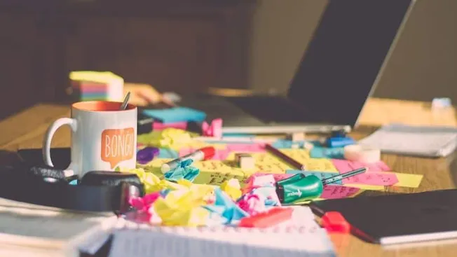 Colorful sticky notes, markers, and office supplies scattered on a cluttered desk with a laptop, representing a creative and