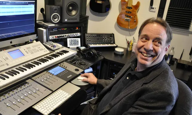 Professional music producer working in a home recording studio with synthesizers, audio equipment, and guitars, creating and