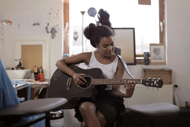 Girl playing acoustic guitar in cozy home music studio, young woman practicing guitar, casual musician, creative workspace, m