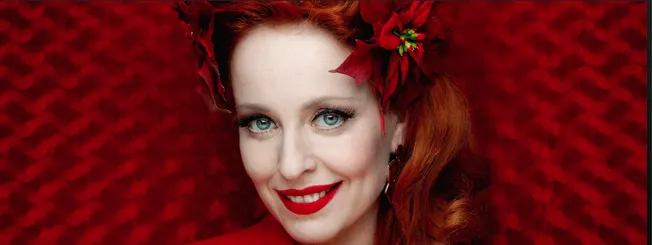 Red-haired woman with vibrant red lipstick and floral headpiece, smiling against a textured red background, vibrant beauty, f