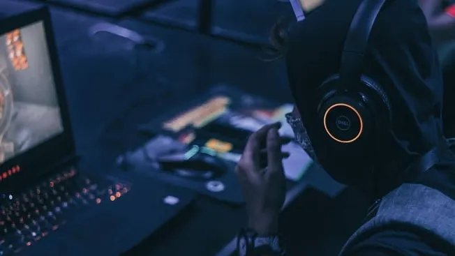 A person wearing headphones working at a laptop with music production equipment, highlighting digital music creation, DJing,