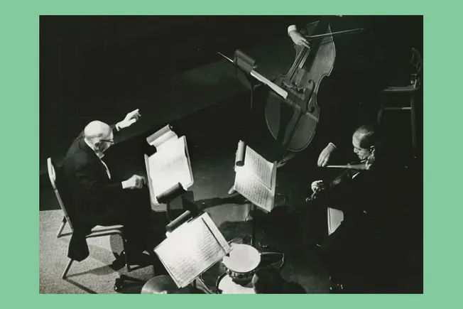 Elderly classical musicians performing a duet with a piano and violin on stage during a concert.