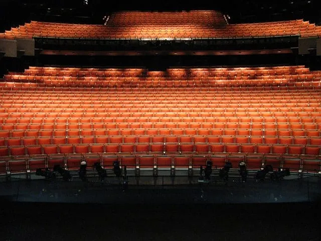 Seats in an empty theater auditorium with orange upholstery and tiered layout, ready for a live performance or event.