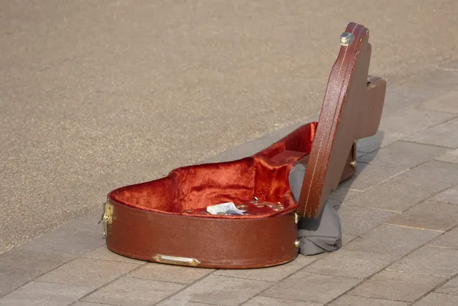 Empty vintage violin case with red velvet interior on a sidewalk, symbolizing lost or abandoned musical instruments, street m