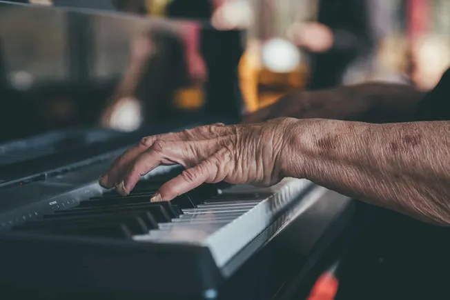 Aged person's hand playing the piano, close-up of elderly hand's fingers on black and white keys, capturing the essence of mu