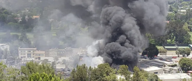 Flaring black smoke rises from a building fire in an urban area with commercial and residential structures, causing significa