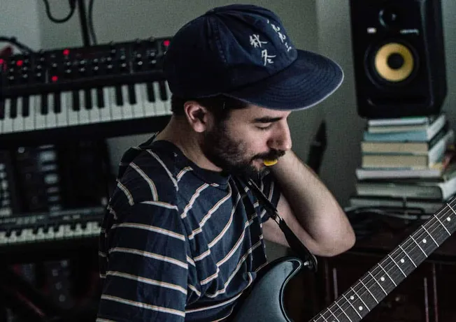 Music producer working in a home recording studio with keyboard and audio equipment, focusing on music production and sound e