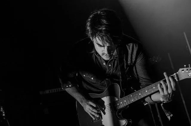 Guitarist performing live on stage with focused expression, playing electric guitar during a concert or music event in a dark