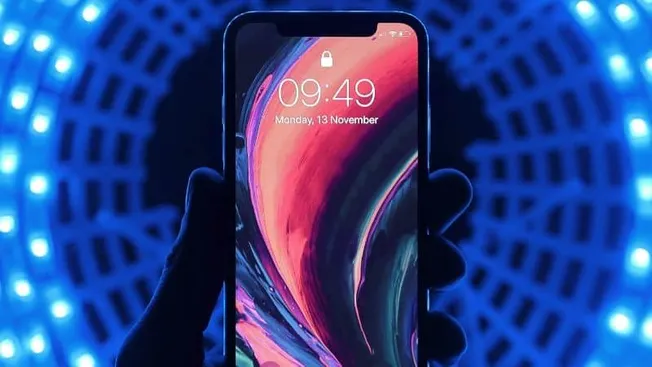 Smartphone displaying time and date, held against vibrant blue LED background, showcasing modern mobile technology.