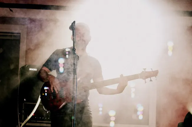 Guitarist performing at a live music venue with stage lighting and fog effects, creating an atmospheric concert scene.