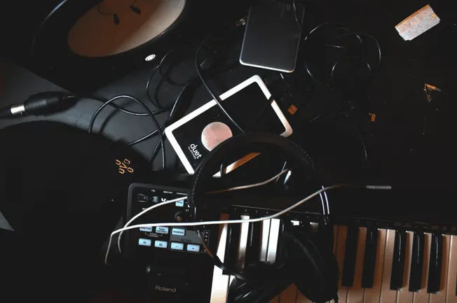 DJ setup with turntable, keyboard, headphones, and electronic devices on a dark music studio desk for music production and li