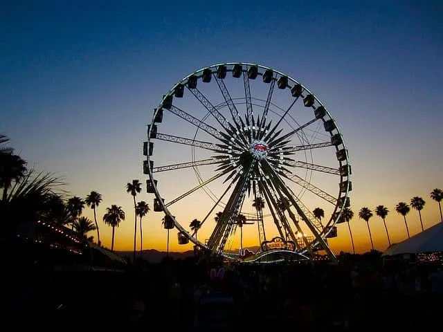 Ferris wheel at sunset during a music festival, with palm trees and tents in the background, capturing a lively outdoor event