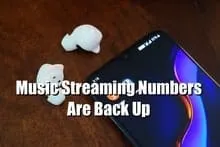 Wireless earbuds next to a smartphone displaying music streaming data, showcasing modern audio technology and digital music c