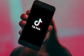 TikTok logo displayed on smartphone screen in hand, showcasing social media streaming app usage.
