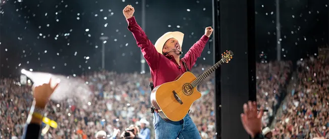 Celebrating a live music performance at a concert with a guitarist passionately playing on stage, surrounded by a large enthu