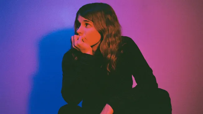Woman in black long sleeve shirt sitting on floor with colorful lighting, music industry concept.