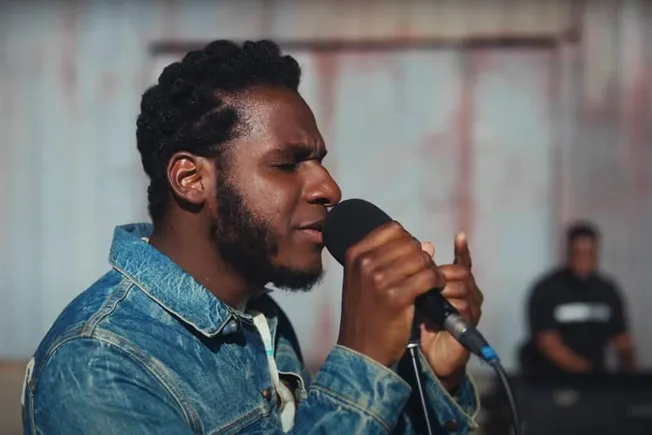 Young African American man passionately singing into a microphone during a live music performance.