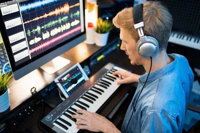 Music producer working on digital audio workstation with keyboard and headphones in home studio, creating music tracks with p