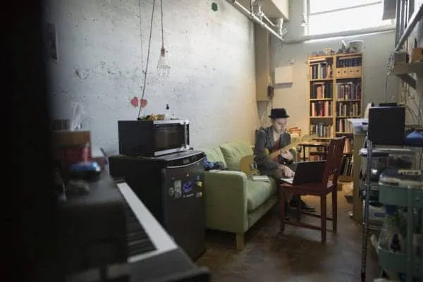 Cozy music studio with a person playing guitar in a well-lit, industrial-style room with bookshelves, sound equipment, and a