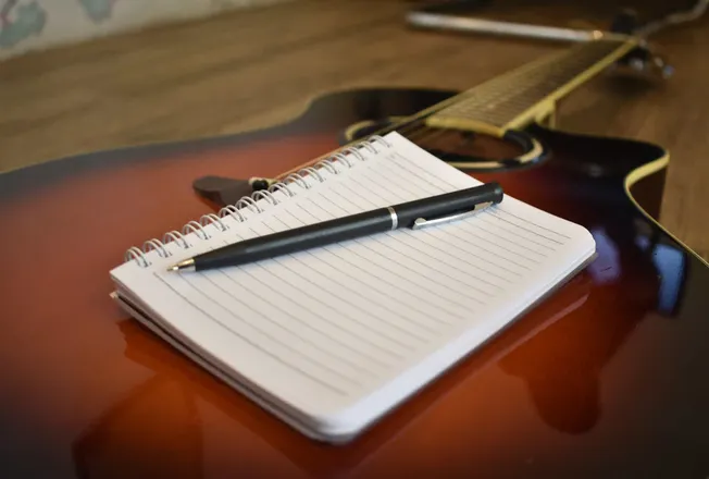 Sheet of lined paper with a black pen on an acoustic guitar; musical planning or songwriting concept.