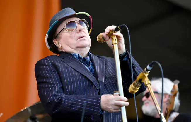 A performer singing into a golden microphone on stage with a musician in the background, showcasing live music performance, j