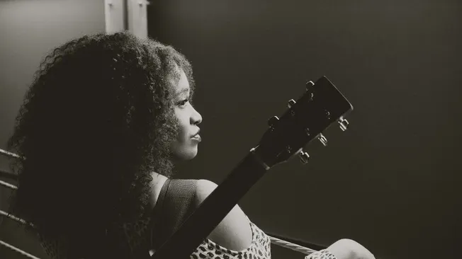 Music artist with curly hair playing guitar in a recording studio, focusing on music production, artist branding, and music i