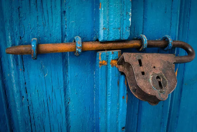 Rustic padlock and latch securing a weathered blue wooden door, symbolizing security and vintage charm, suitable for articles