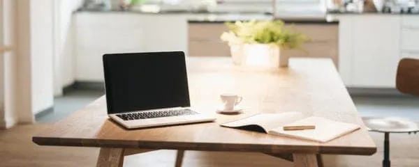 Laptop on a modern kitchen table with a cup, open notebook, and pen, representing digital music industry insights and media c