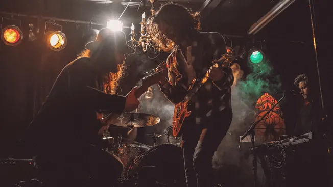 Musicians playing guitars on stage during live concert with colorful stage lights, capturing energetic underground music perf