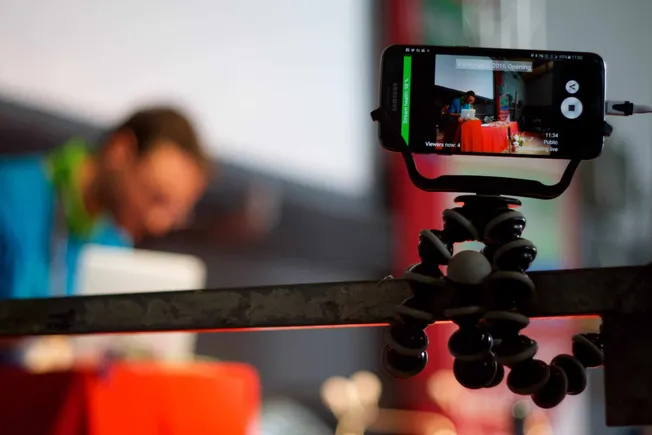 Mobile phone on a flexible tripod recording a live event with a woman at a table, capturing music industry content, streaming