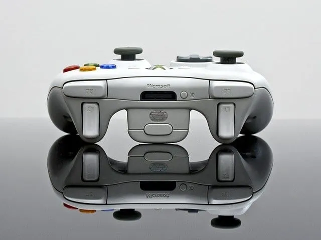 Gaming controller on reflective surface, close-up of white Microsoft Xbox controller with colorful buttons, used for gaming a